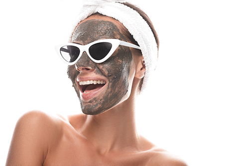 nude young woman in cosmetic hair band and sunglasses with clay mask on face laughing isolated on white