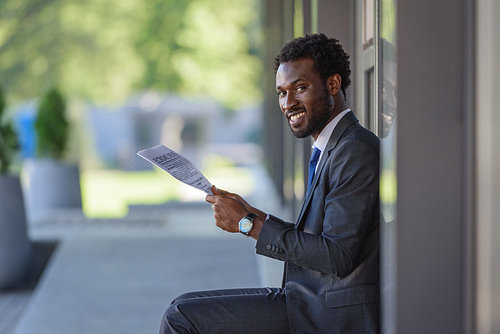 handsome african american businessman holding newspaper and smiling at camera