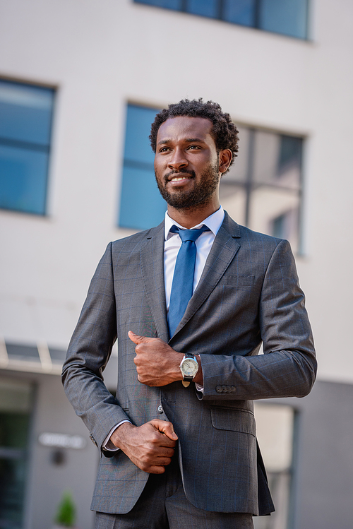 positive african american businessman in suit smiling and looking away