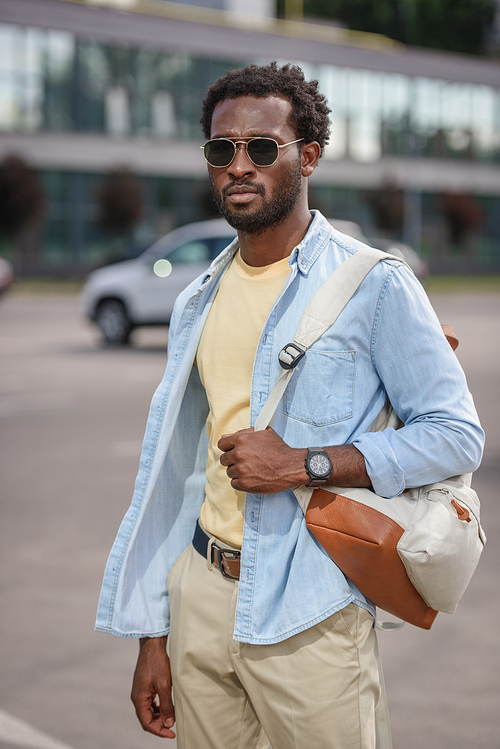 handsome african american man in sunglasses standing at car parking