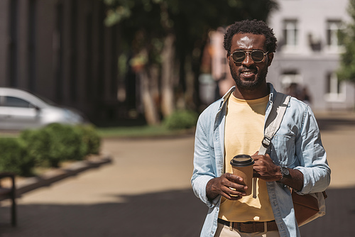handsome, stylish african american man in glasses holding paper cup while 