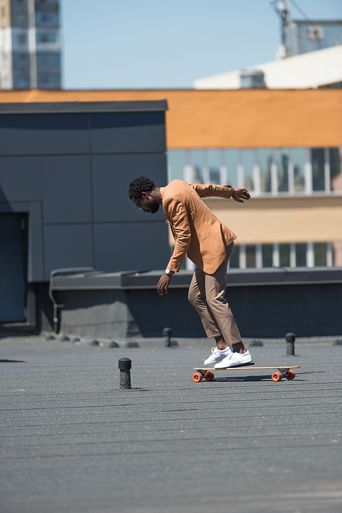 stylish african american businessman riding longboard on rooftop