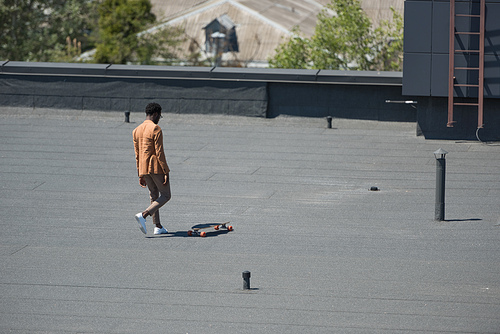 stylish african american businessman in walking on rooftop with longboard