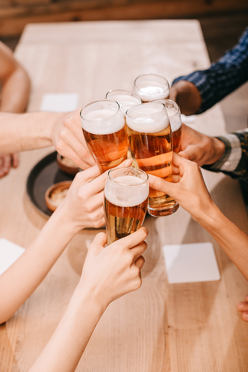 partial view of multicultural friends clinking glasses with lager beer in pub