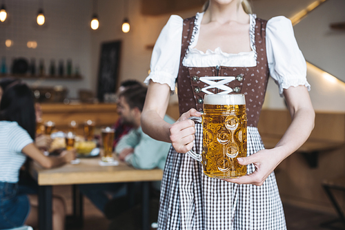 patial view of  waitress in german national costume holding mug of light beer