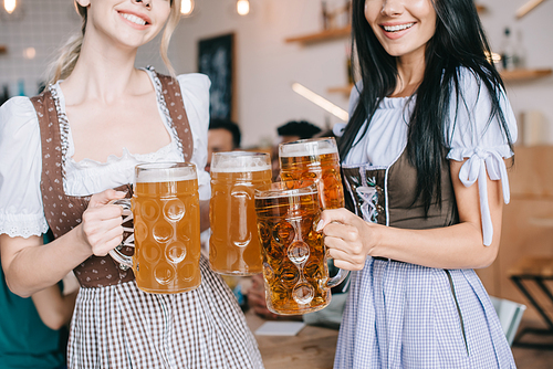 cropped view of two young waitresses in traditional german costumes holding mugs with beer