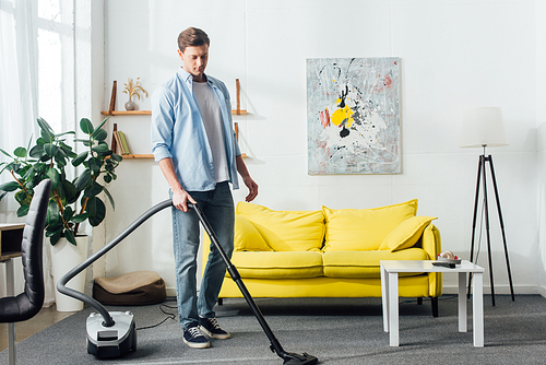 Man cleaning carpet with vacuum cleaner in living room