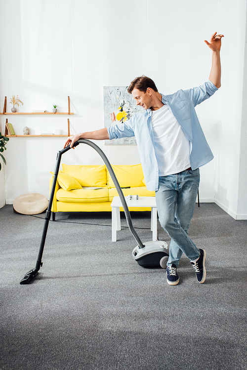 Handsome man cleaning carpet in living room with vacuum cleaner