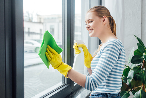 Side view of attractive woman cleaning glass of window with rag and detergent