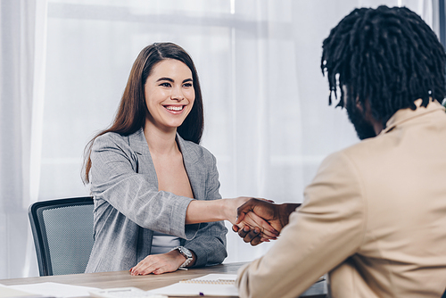 Selective focus of employee smiling and shaking hands with african american recruiter at job interview in office