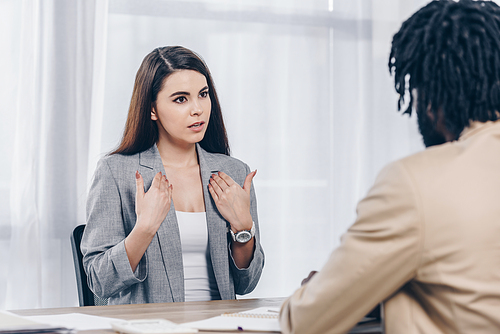 Selective focus of employee pointing oneself and talking to african american recruiter at job interview in office