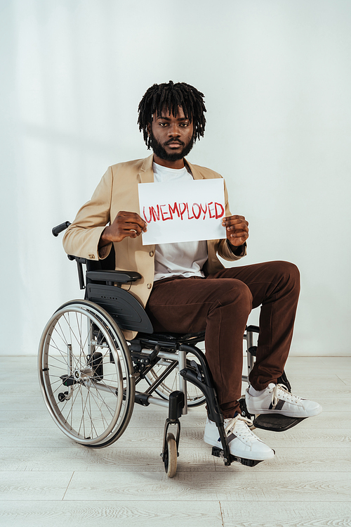 Disabled african american man  with placard with unemployed lettering on wheelchair on white