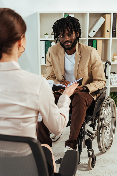 Selective focus of recruiter and african american disabled employee with notebook talking and looking at each other