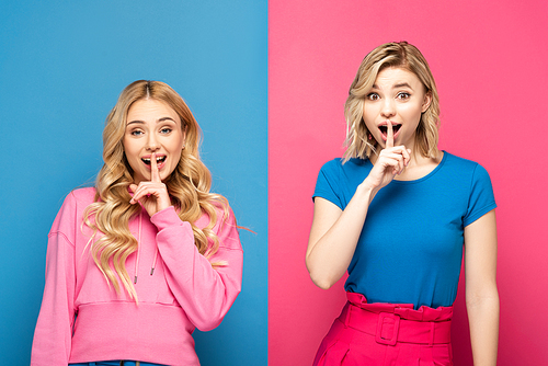 Excited blonde sisters showing silence sign at camera on pink and blue background