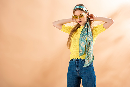 beautiful stylish girl posing in jeans, yellow t-shirt, sunglasses and silk scarf on beige