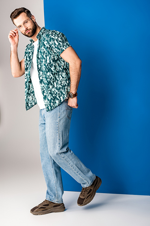 handsome bearded man posing in summer clothes and sunglasses on grey and blue