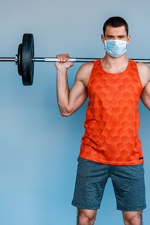 sportsman in medical mask exercising with barbell isolated on blue