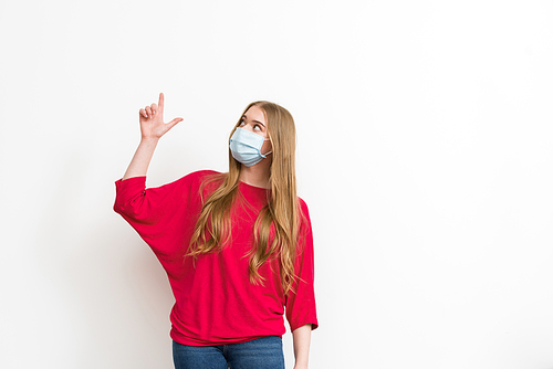 woman in medical mask pointing with finger and looking up isolated on white