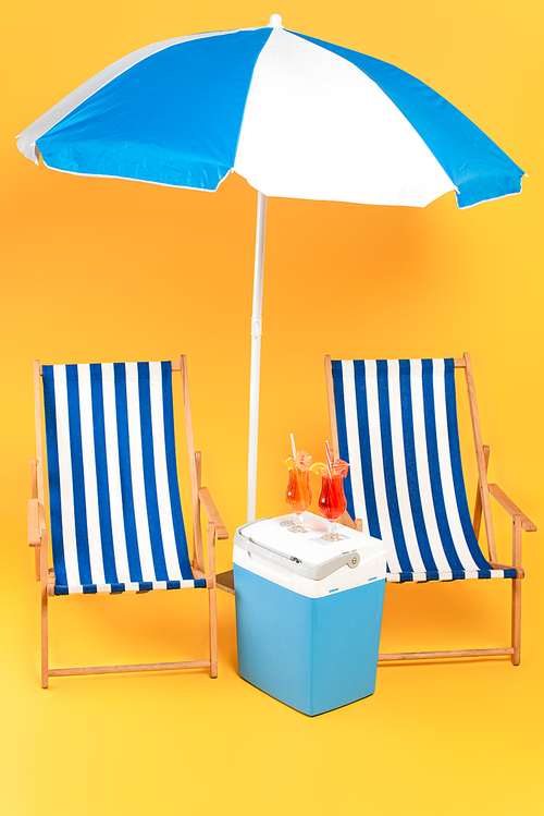 deck chair near beach umbrella and cocktails on portable fridge freezer on yellow
