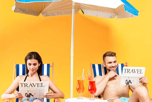 happy couple reading travel newspapers and sitting on deck chairs on yellow
