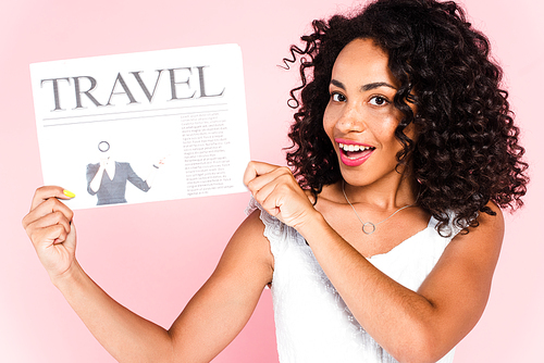 excited african american woman holding travel newspaper isolated on pink