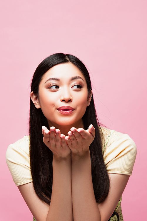 young asian woman sending air kiss and looking away isolated on pink