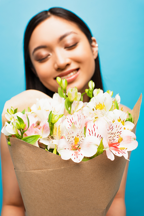 selective focus of bouquet of flowers near happy asian girl with closed eyes on blue