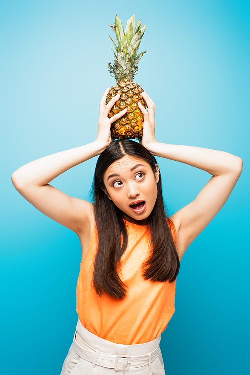 emotional asian girl holding ripe pineapple on blue