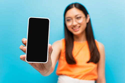 selective focus of happy asian girl holding smartphone with blank screen isolated on blue