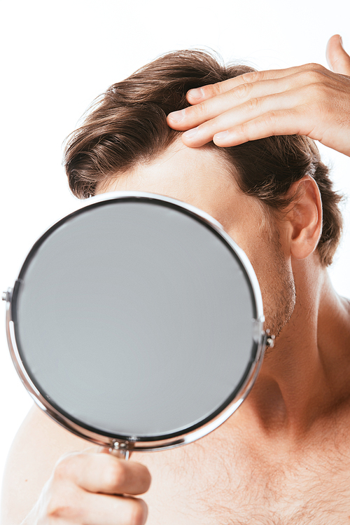 Selective focus of shirtless man touching hair while holding mirror isolated on white