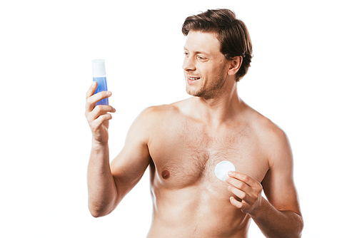 Shirtless man looking at bottle of toner while holding cotton pad isolated on white