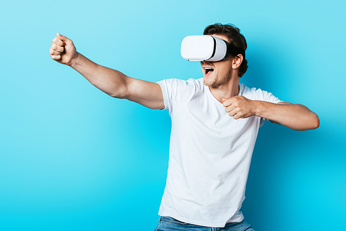 Young man in white t-shirt gesturing while using vr headset on blue background