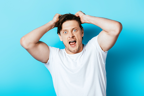 Crazy man with hands near hair in white t-shirt  on blue background