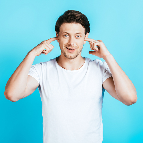 Man in white t-shirt covering ears with fingers on blue background