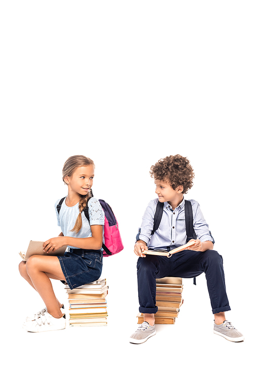 schoolkids sitting on books and looking at each other isolated on white