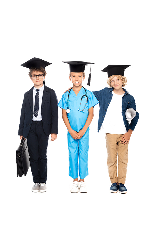 kids in graduation caps dressed in costumes of different professions standing with stethoscope, blueprint and briefcase isolated on white