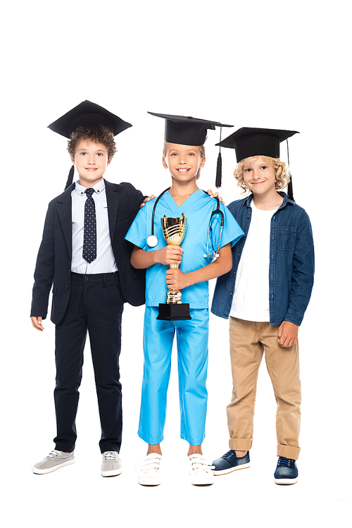 children in graduation caps dressed in costumes of different professions holding trophy isolated on white