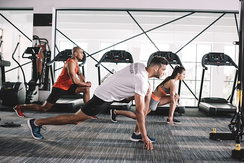 handsome trainer doing lunges exercise together with multicultural athletes