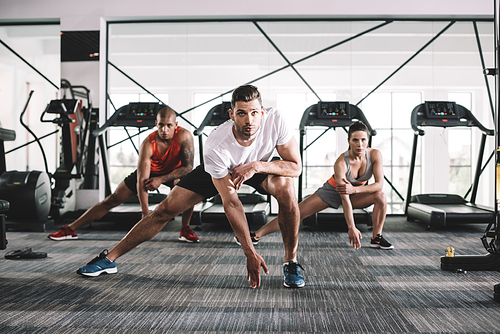 handsome trainer  while doing lunges exercise together with multicultural athletes