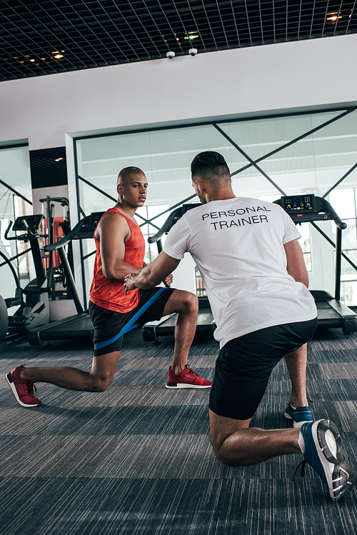 back view of personal trainer instructing african american sportsman exercising with expander