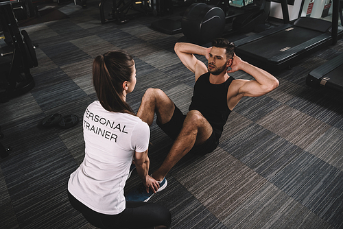 young trainer supporting handsome sportsman doing push ups