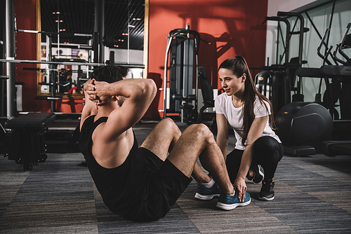 attentive trainer supporting handsome sportsman doing push ups