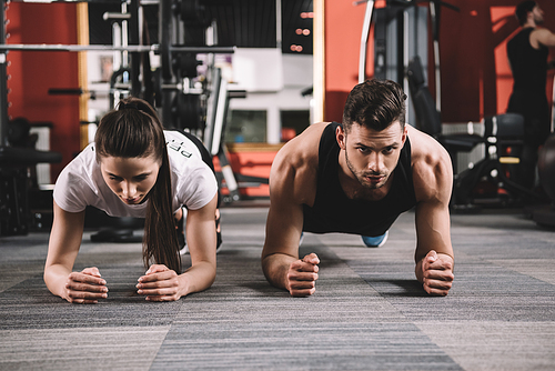 attractive trainer doing plank exercise together with handsome sportsman