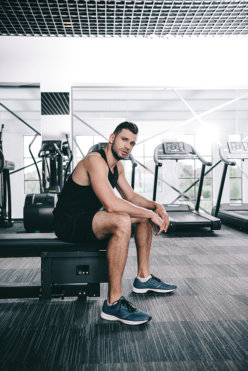 handsome, young sportsman  while sitting on treadmill in gym