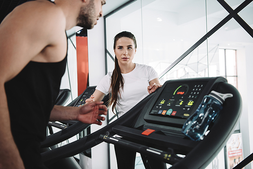 attentive trainer looking at sportsman running on treadmill