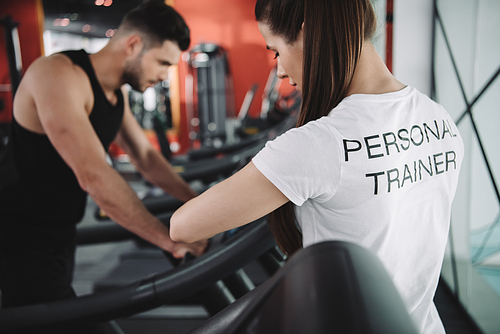 selective focus of personal trainer standing near sportsman running on treadmill