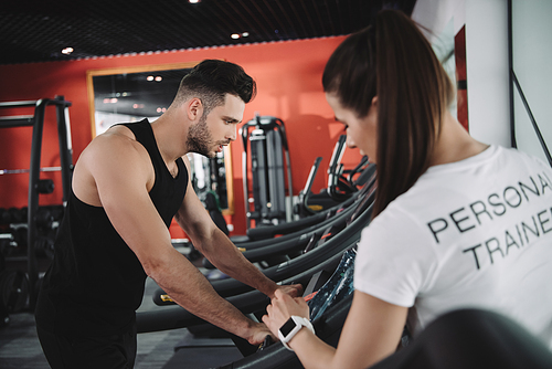 selective focus of personal trainer standing near sportsman running on treadmill