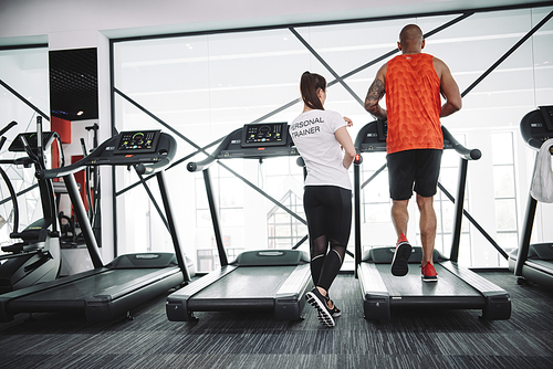 back view of personal trainer supervising african american sportsman running on treadmill