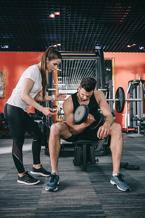 attractive trainer instructing young sportsman working out with dumbbell
