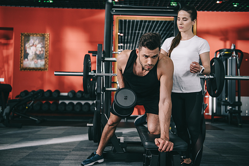attractive trainer assisting handsome sportsman working out with dumbbell